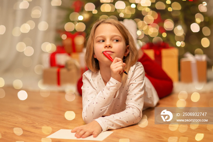 christmas, holidays and childhood concept - girl writing wish list or letter to santa at home