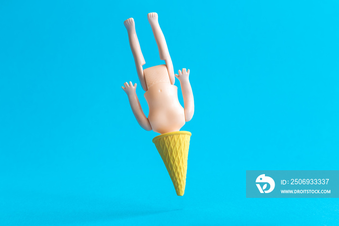 Doll stuck into ice cream cone abstract isolated on blue.