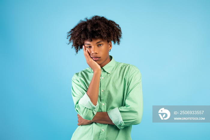 Portrait of black teen guy feeling bored, leaning on his hand, having dull day on blue studio backgr