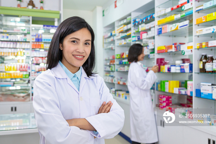 Smiling Asian female pharmacist in the modern drugstore with her workmate.