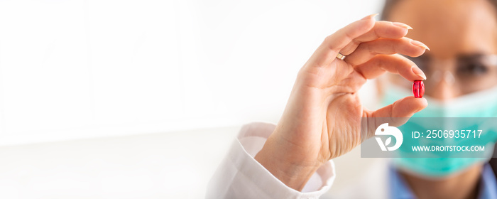 Young female scientist holding a red pill - close-up