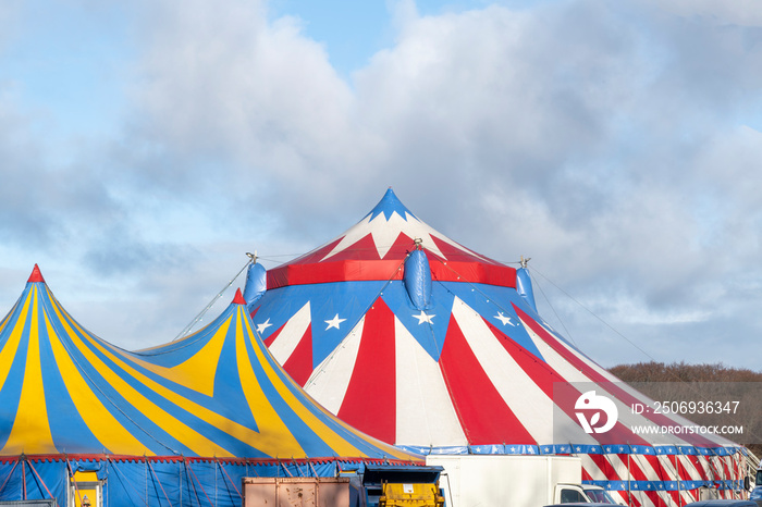 Red and white circus tent topped with bleu starred cover against a sunny blue sky with clouds