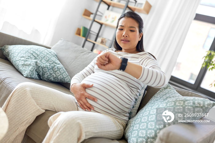 pregnancy, rest, people and expectation concept - pregnant asian woman with smart watch having labor