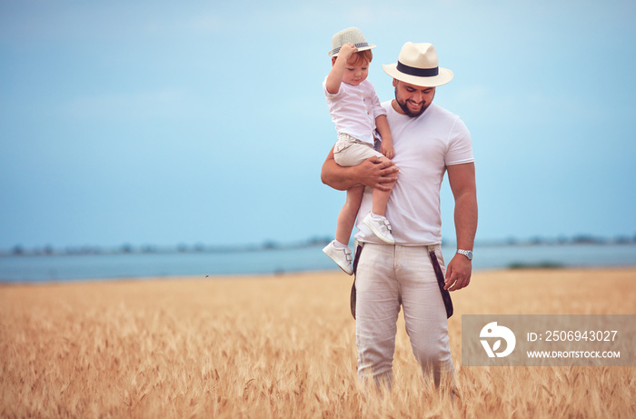 happy father with toddler son walking through the ripe wheat field