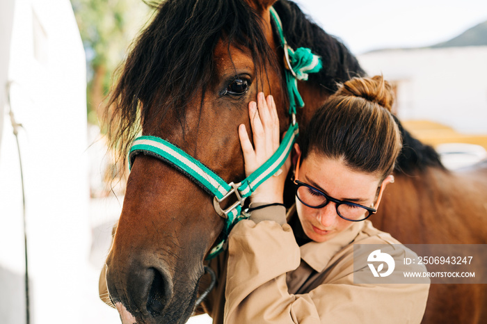 Young woman physiotherapist taking care a brown horse.