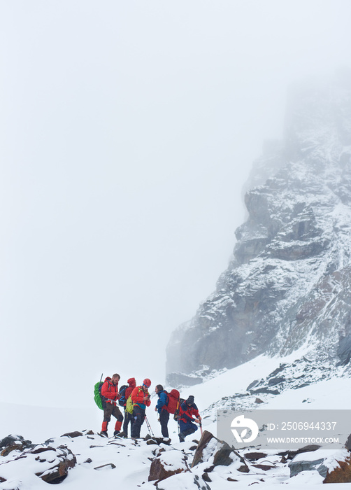 徒步旅行队站在被雪覆盖的高山附近的岩石小路上。带着背包的男性旅行者