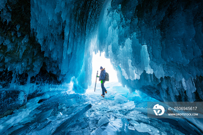 一名游客或摄影师在俄罗斯贝加尔湖上令人惊叹的冰洞里旅行。冬季蓝色背景