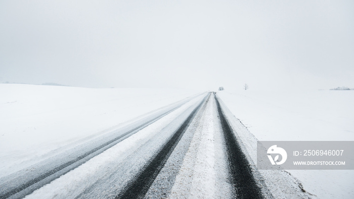 Snow-covered highway (asphalt road) through the country fields in a fog after a blizzard. Dangerous 