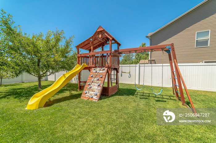 Wooden playground structure with yellow plastic slide swings and climbing wall