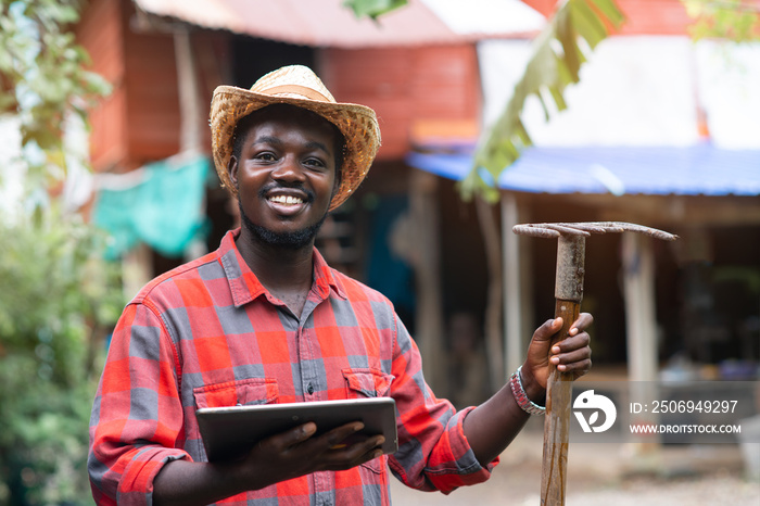 Happiness african male farmer stands and using tablet with his farmhouse in the background.