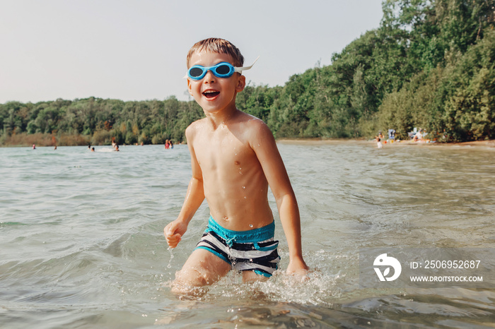 Cute funny Caucasian boy swimming in lake with underwater goggles. Child diving in water on a beach.