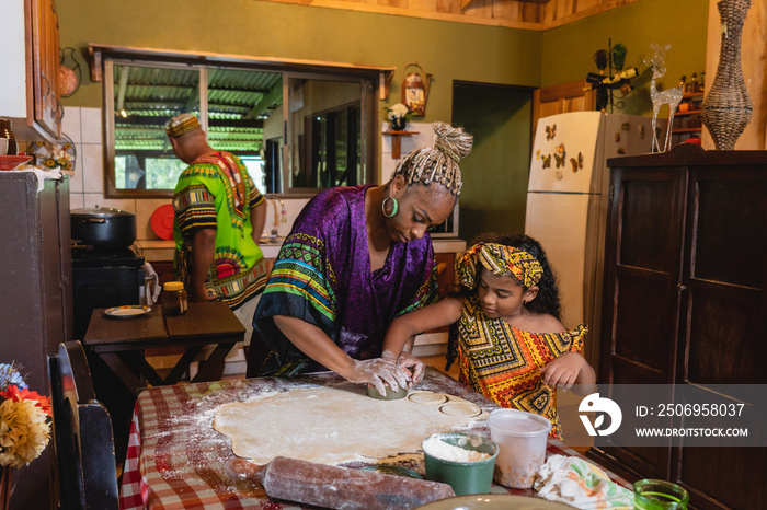 Imagen horizontal de una madre afrocaribeña en el interior de su hogar, cocinando junto a su pequeña