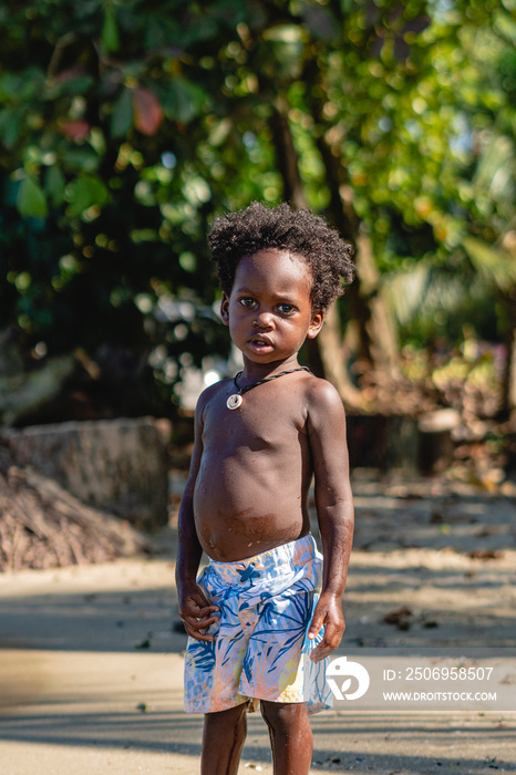 imagen vertical de un niño moreno con cabello afro y sin camisa viendo a cámara serio en un hermoso 