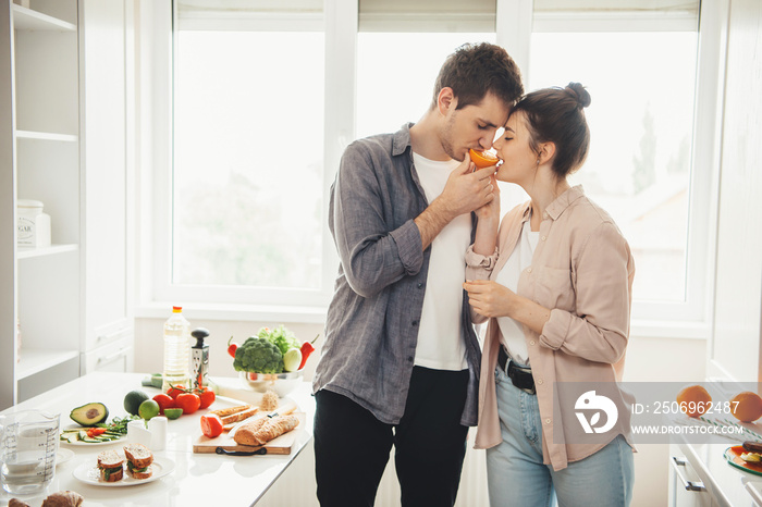 一对年轻的高加索夫妇一起准备食物，正在用橙子咬