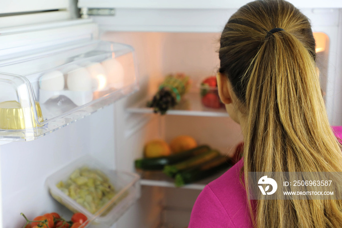 Back view of young woman looks inside the fridge searching for healthy food