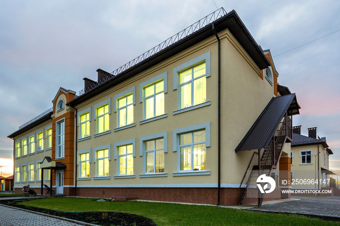 New modern two-storied kindergarten preschool building,green grassy lawn and paved sidewalks on blue