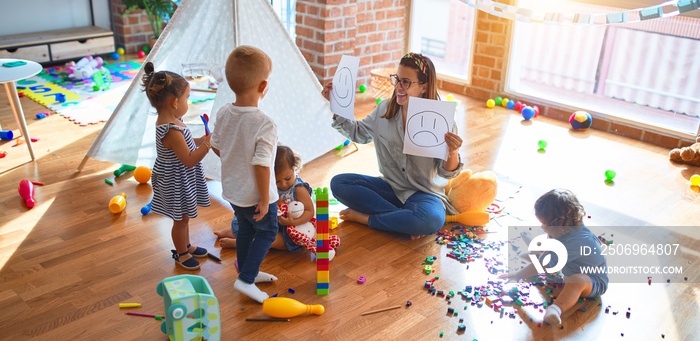 Beautiful psychologist and group of toddlers make therapy using emotions emojis around lots of toys 