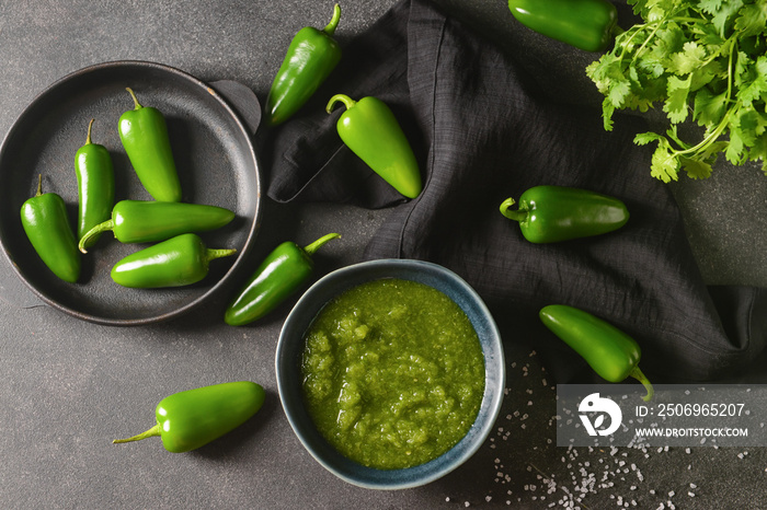 Bowl of Tomatillo Salsa Verde sauce and jalapeno pepper on dark background