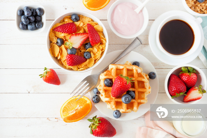 Breakfast food table scene. Fruits, cereal, waffles, yogurt, milk and coffee. Top view over a white 