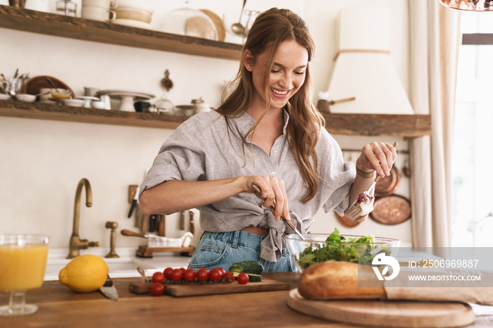 Happy positive cute beautiful woman indoors at the kitchen cooking.