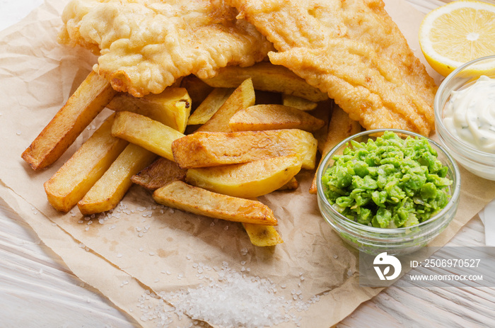 Traditional British street food fish and chips with tartar sauce and mushy peas on paper plate