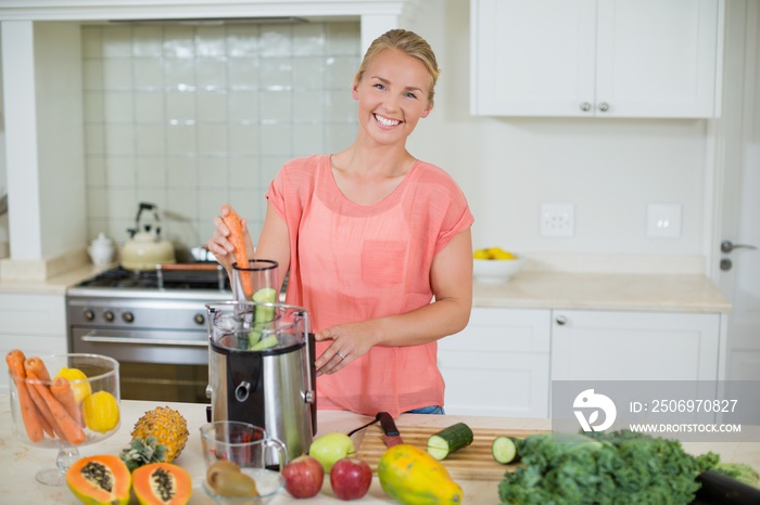 Smiling woman preparing fresh fruit juice in kitchen