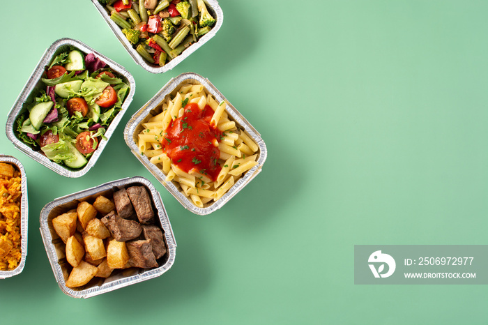 Take away healthy food in foil boxes on green background. Top view. Copy space