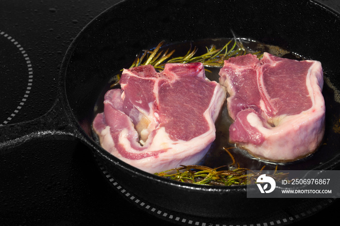 Lamb loin chops with rosemary in a cast iron frying pan.  Cooking on an electric hob stove