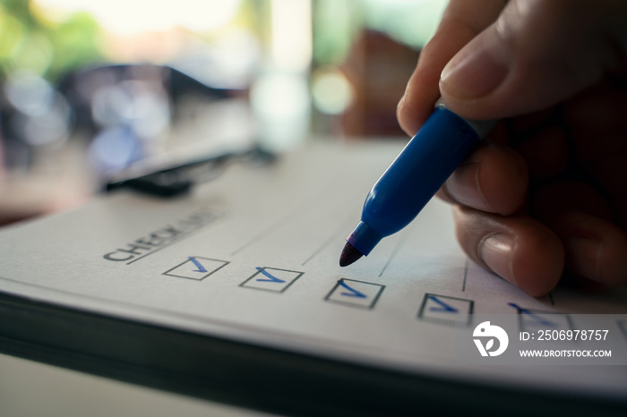 Hand with blue pen marking on checklist box.