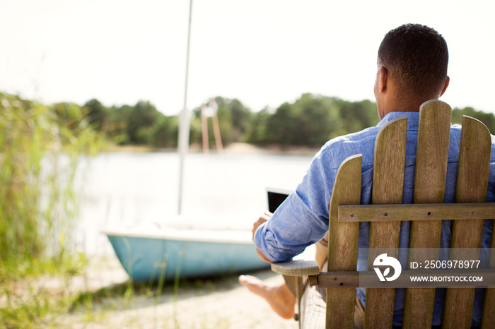 Man with tablet pc sitting in chair by river