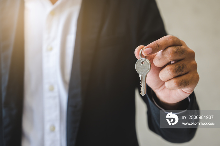 Close up business hand holding key in house.