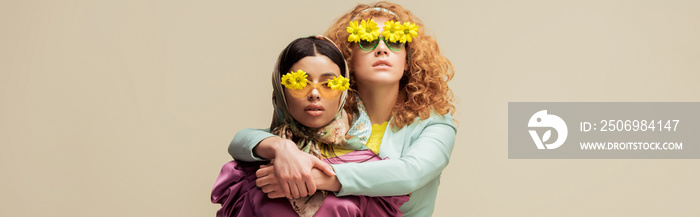 panoramic shot of attractive african american girl and curly redhead woman in sunglasses with flower