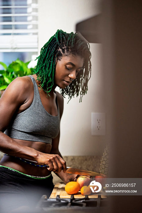 Black woman with green dreadlocks cleaning and eating fruit in her kitchen