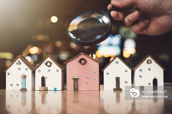 Hand holding magnifying glass and looking at house model, house selection, real estate concept.