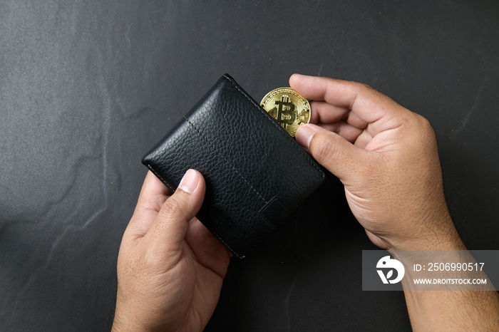 Businessman putting bitcoin into a black leather wallet on black background. saving bitcoin