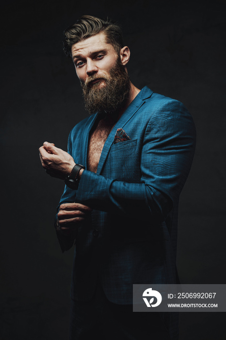 Bearded and serious business person dressed in blue custom suite posing holding his jacket sleeve in