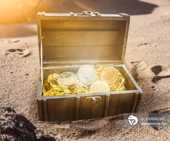 treasure chest filled with bitcoins surrounded by golden glow partially burried in sand on beach