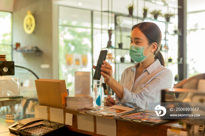 Woman customer with protective mask paying bill by cell phone in cafe.