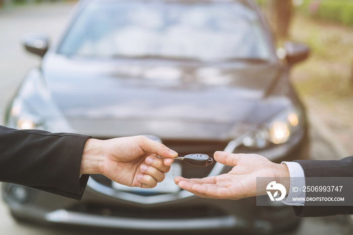 Car key, businessman handing over gives the car key to the other woman on car background.