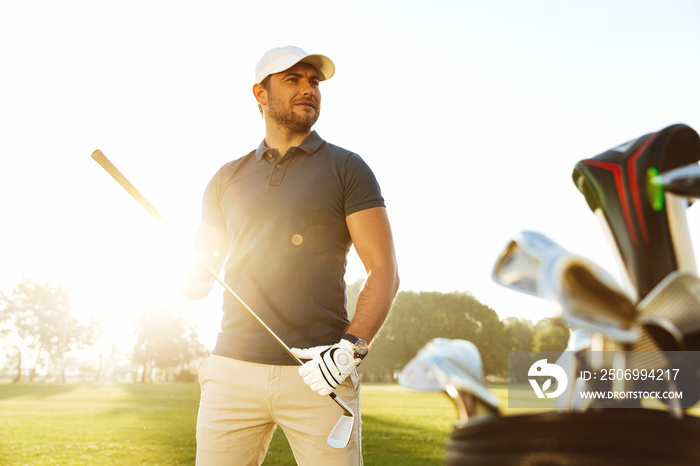 Young man carrying golf club while standing on field