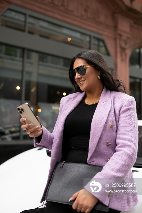 Young businesswoman leaning against luxury car and using phone