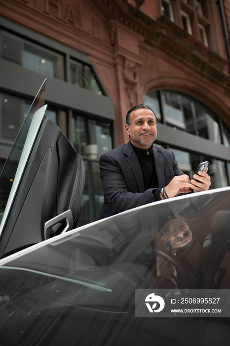 Mature man standing by luxury car and using phone