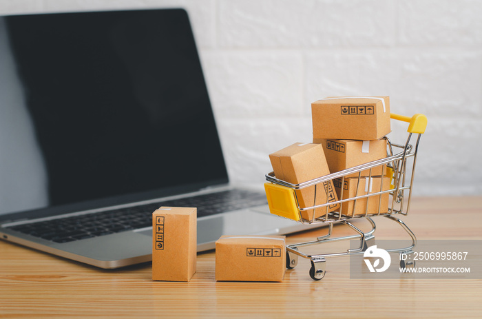 Online shopping and delivery service concept.Brown paper boxs in a shopping cart with laptop on wood