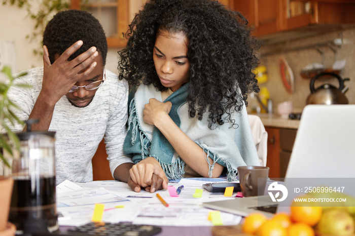 Young African-American couple with many debts calculating gas and electricity bills while doing pape