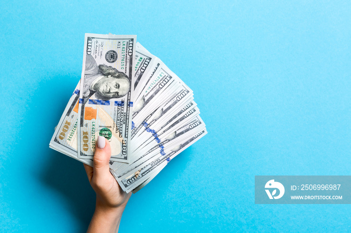 Top view of female hand holding a fan of money on colorful background. One hundred dollar bills. Cre