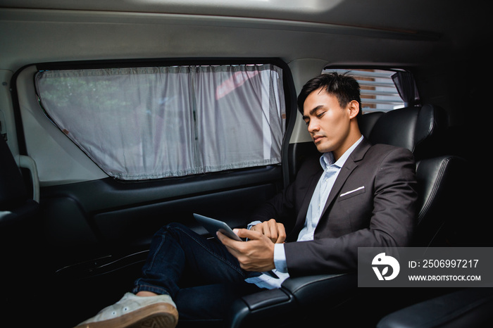 asian young businessman with tablet sitting on passenger seat of his luxury car