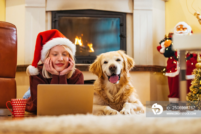 Modern young woman spending Christmas morning at home relaxing on floor with her dog in living room 