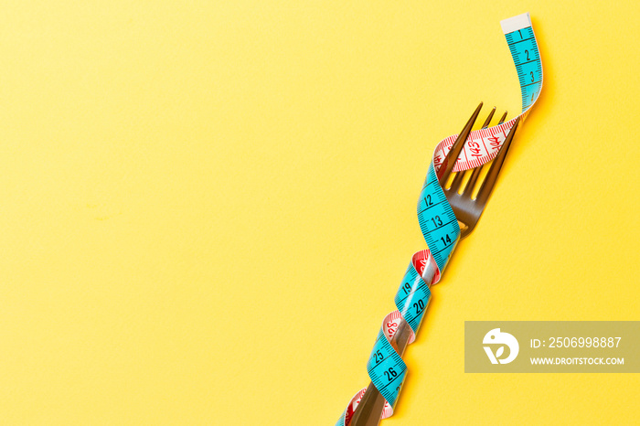 Diet and healthy eating concept with wrapped fork in measuring tape on yellow background. Top view o