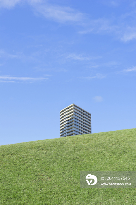 A tall modern office building, rising above a grass ridge