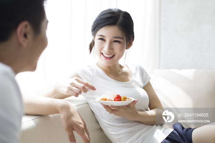 快乐的年轻夫妇在沙发上吃水果沙拉